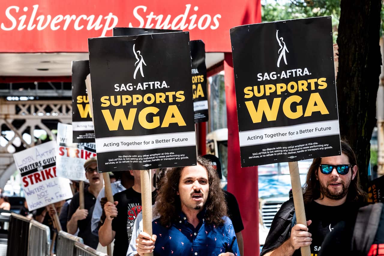 People walking with signs saying "Writers Guild on Strike" and "SAG-AFTRA Supports WGA" in front of Silvercup Studios.