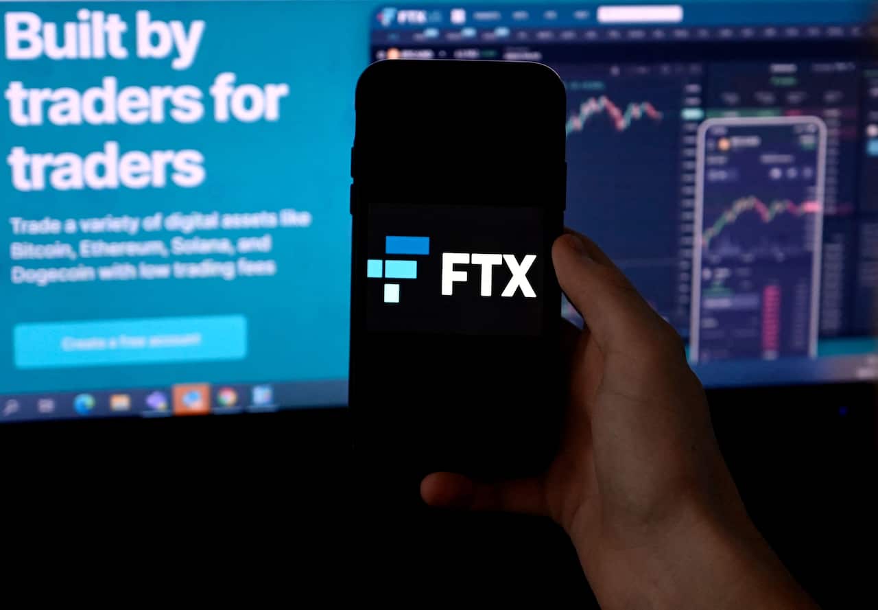 A smartphone with the FTX symbol on it and a monitor in the background.