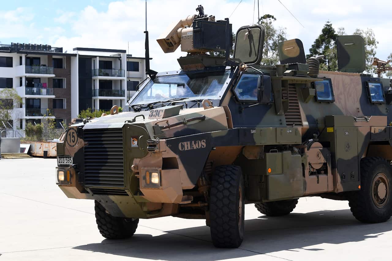 A Bushmaster vehicle with camouflage print, driving down a street.