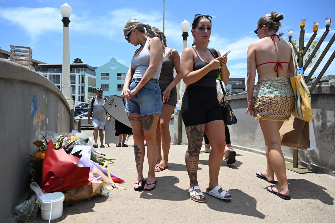 People walk over the pedestrian bridge, some stopping to look at tributes.