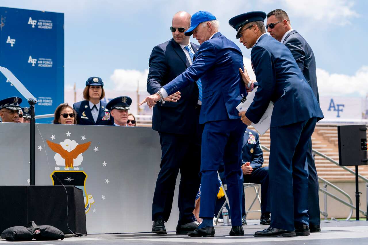 Joe Biden points at a sandbag on the ground as three members of his security entourage stand around him.