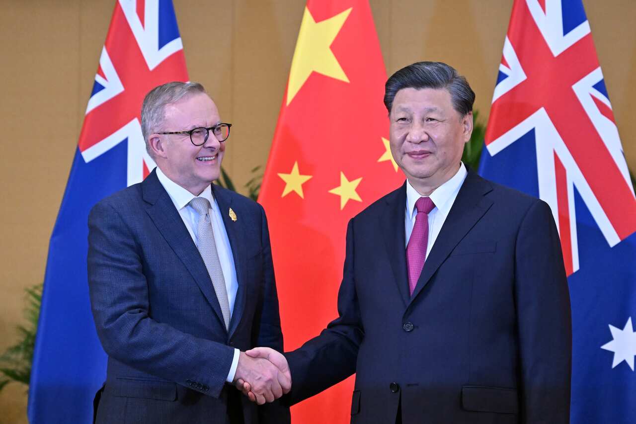 Anthony Albanese and Xi Jinping shake hands in front of the Chinese and Australia flags.