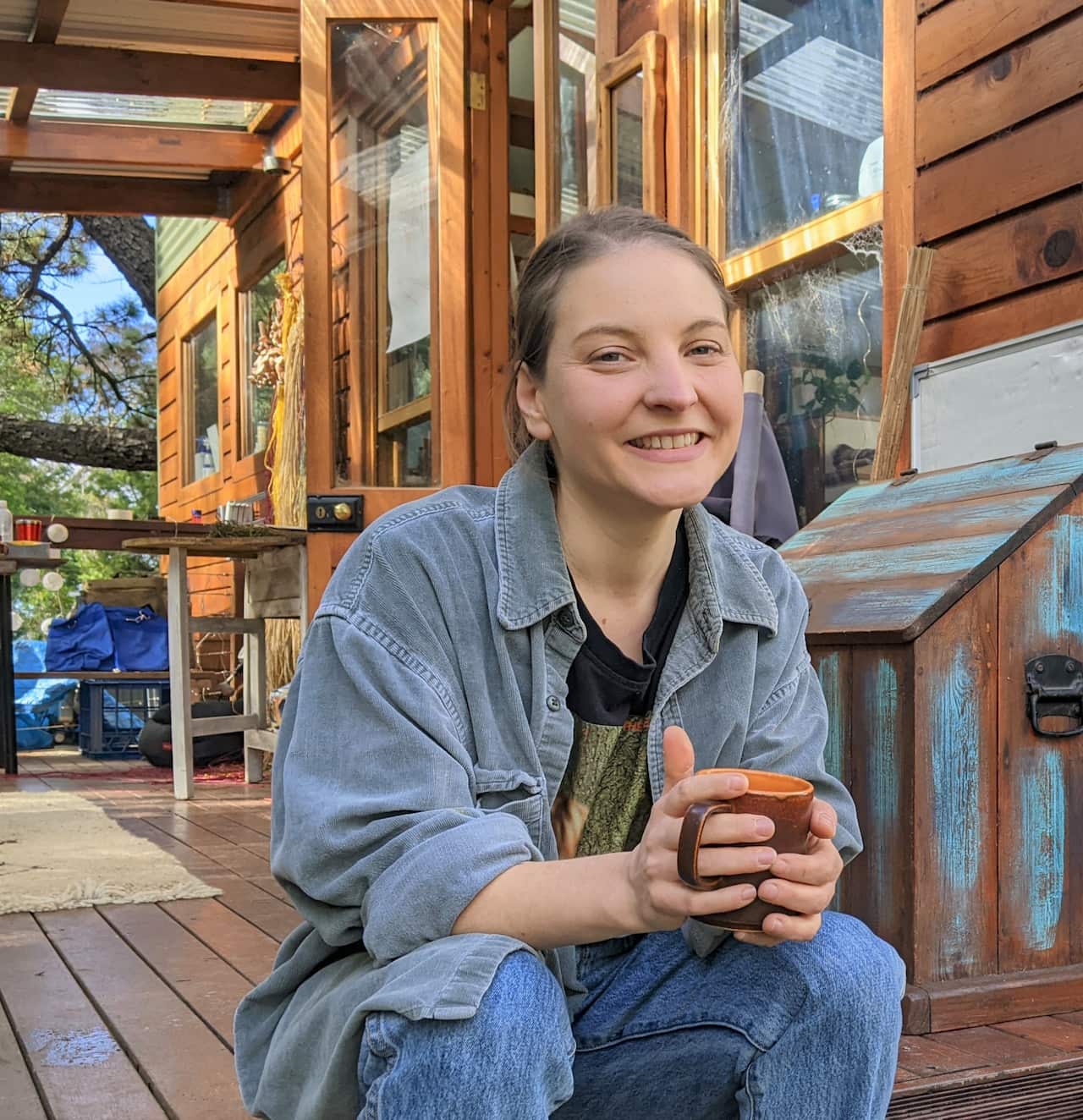 A woman sitting with a cup of tea at her tiny house in the mountains.