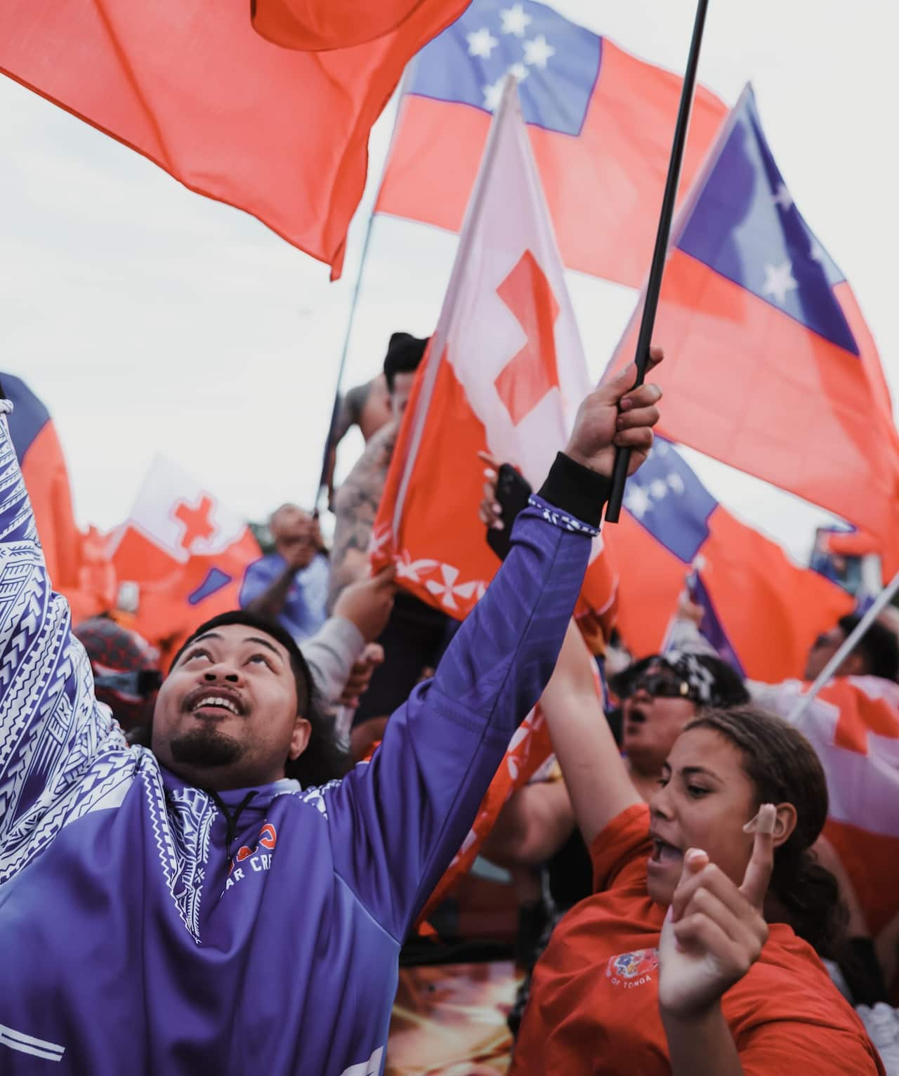 A man holds up a Samoa flag, with Tongan flags in the background. 