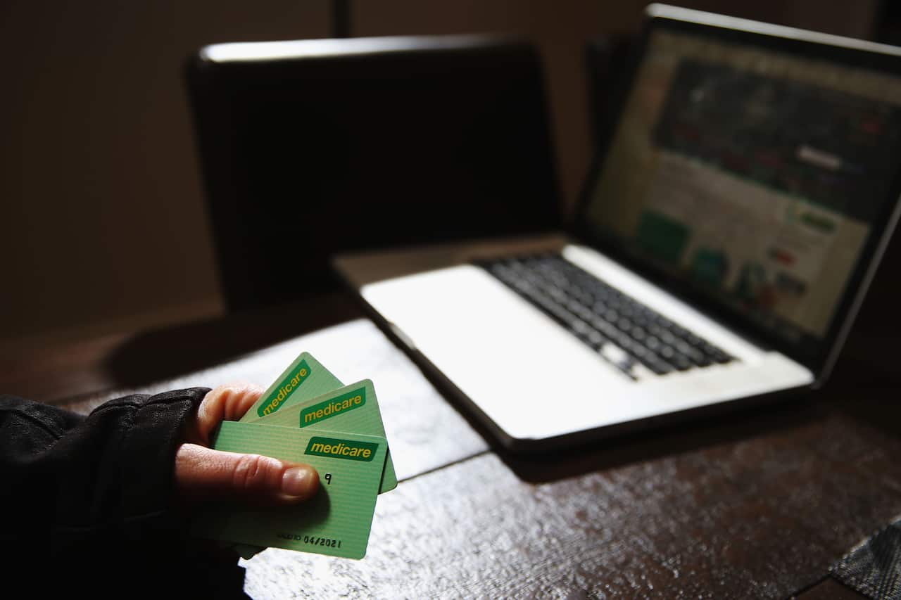 A hand in a black sleeve holding three green cards in front of a laptop