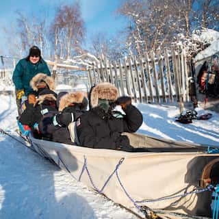 people wearing fur hats sitting in a canvas dog sled on the snow