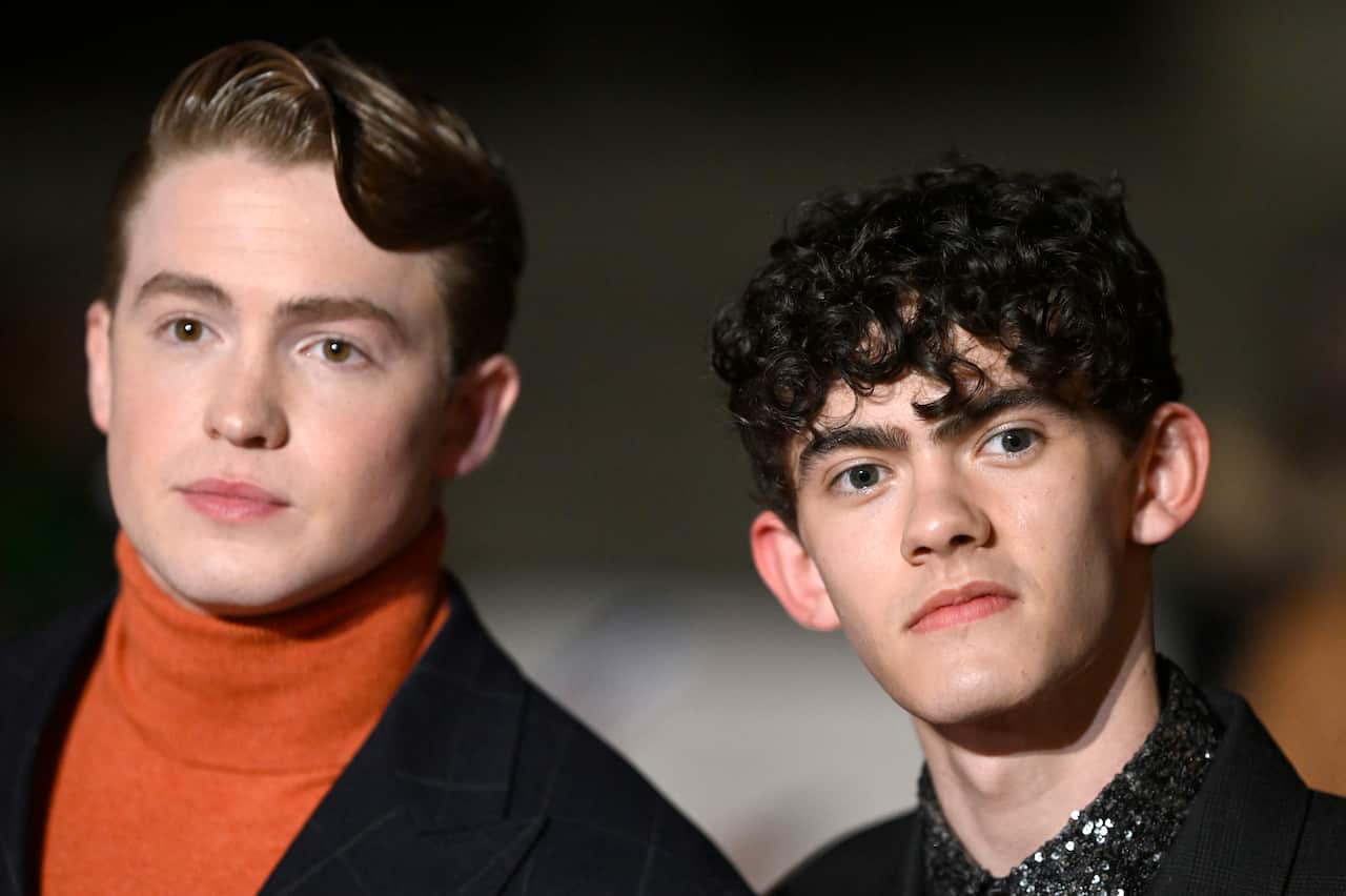 A brunette male and a red-haired male stand side by side.