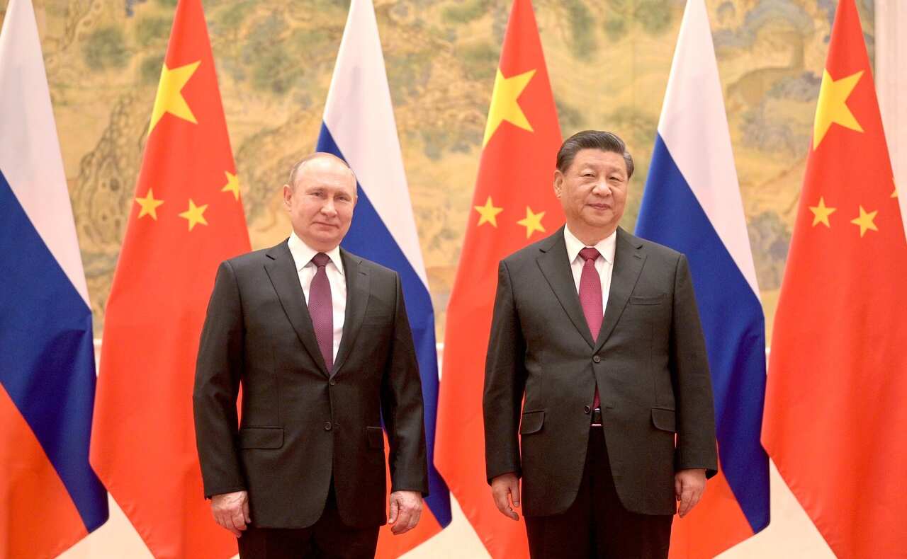 Two men standing in front of Russian and Chinese flags.