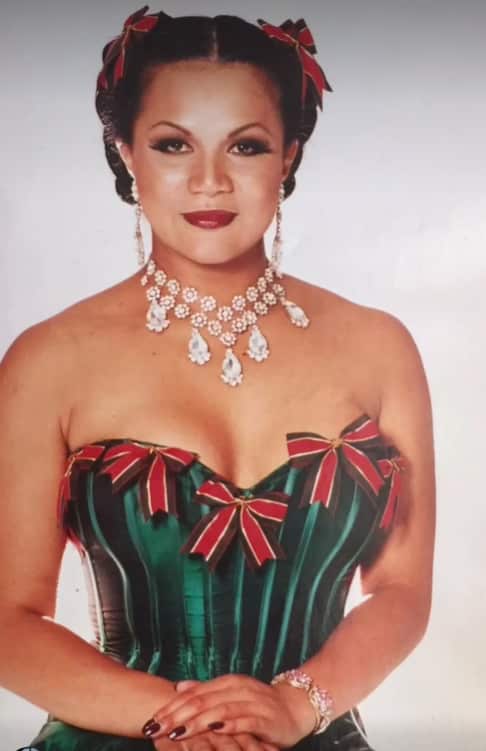 A portrait shot of a woman wearing a big crystal necklace and green and red dress