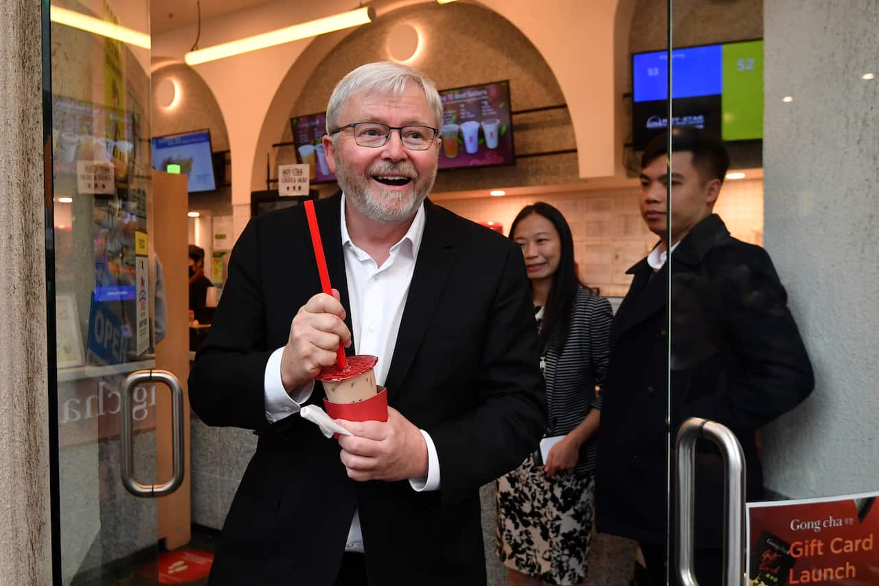A man wearing a suit smiles while holding a straw and plastic cup of bubble tea