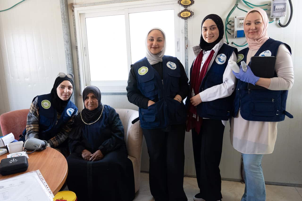 Five female health officers wearing matching navy blue vests pose for a photo in a light-filled room. 