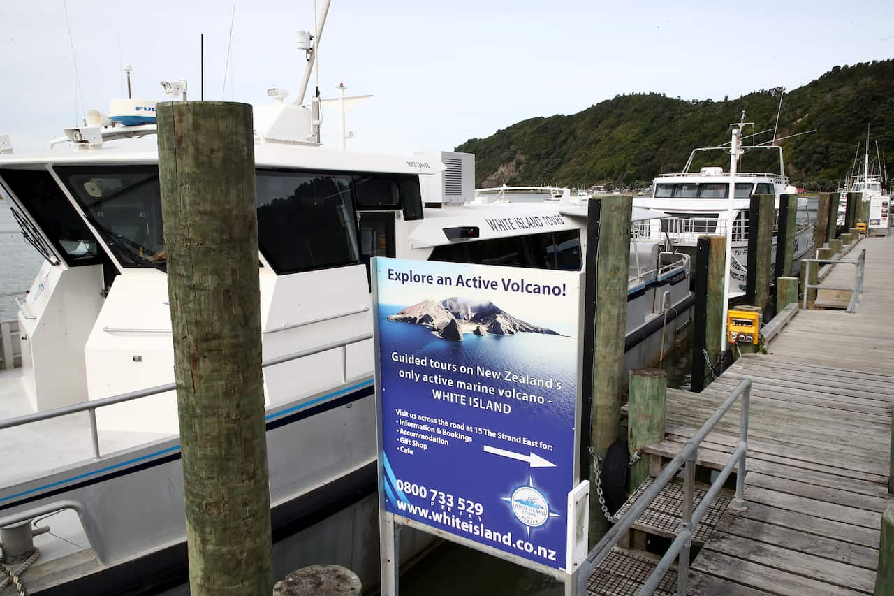 Three boats are seen on a wharf with a placard for White Island Tours that reads "Explore an Active Volcano!"