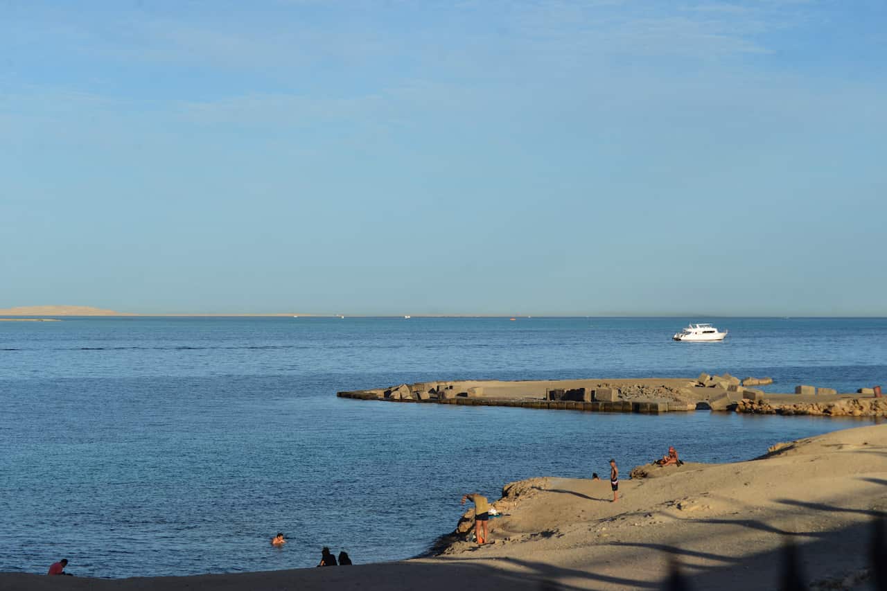 A boat in the distance with people standing and swimming along the coastline.