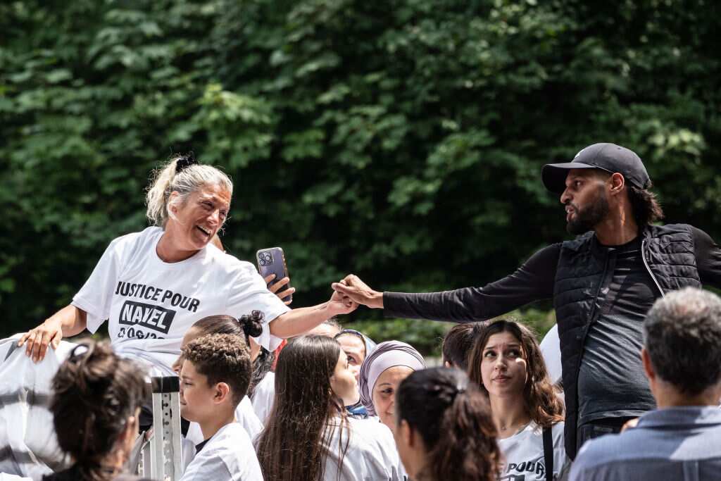 A woman and a man look at each other and hold hands in unison surrounded by other people, who are united in protest over the shooting of teen Nahel M in Paris.
