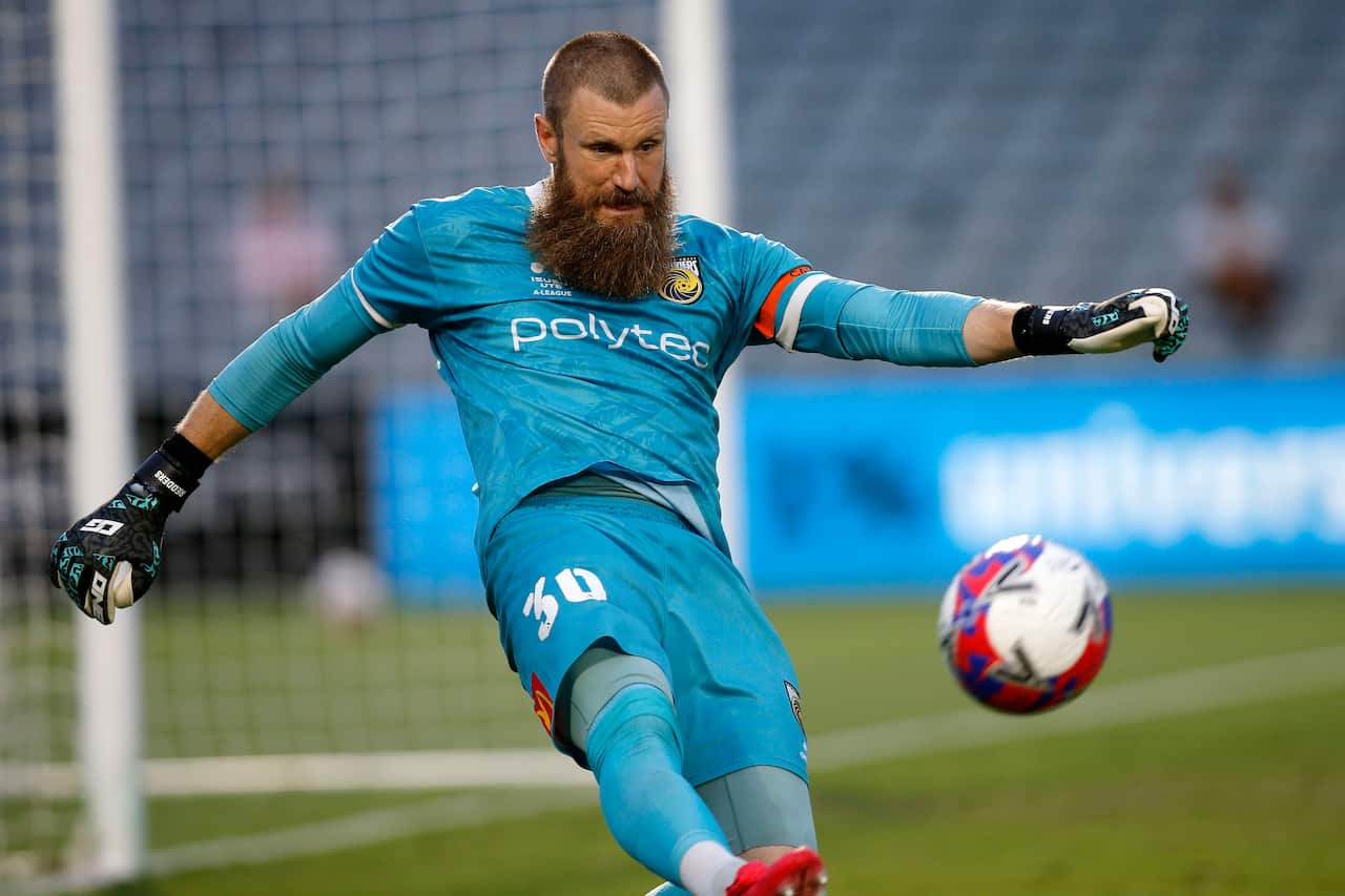 A bearded goalkeeper in a teal jersey and shorts kicks a ball down the field during a match.