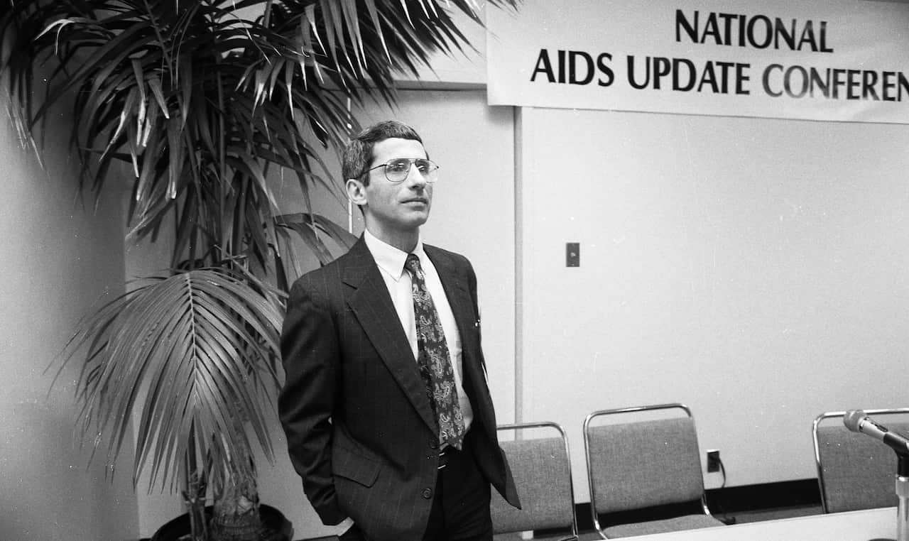 Dr. Anthony Fauci standing in a room with a sign that says "National AIDS Update Conference".