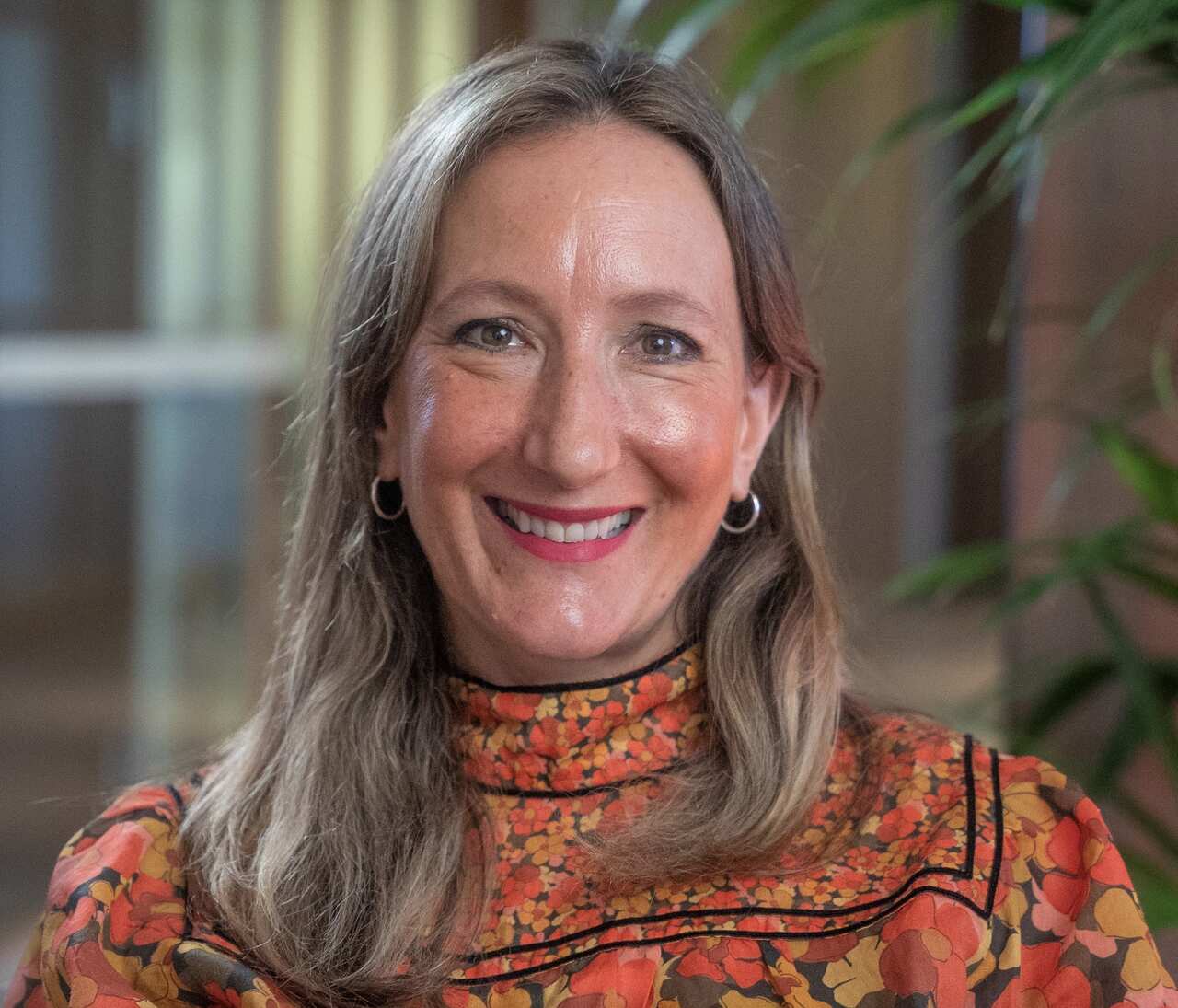Melanie Greblo in an orange shirt sitting near a palm plant.