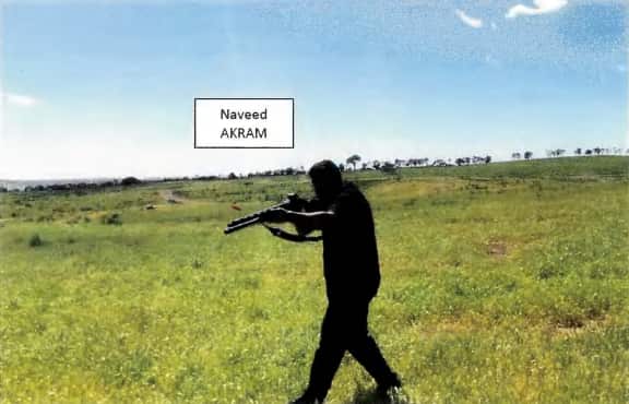 A man holding up a shotgun in a paddock. The picture has a label - Naveed Akram 