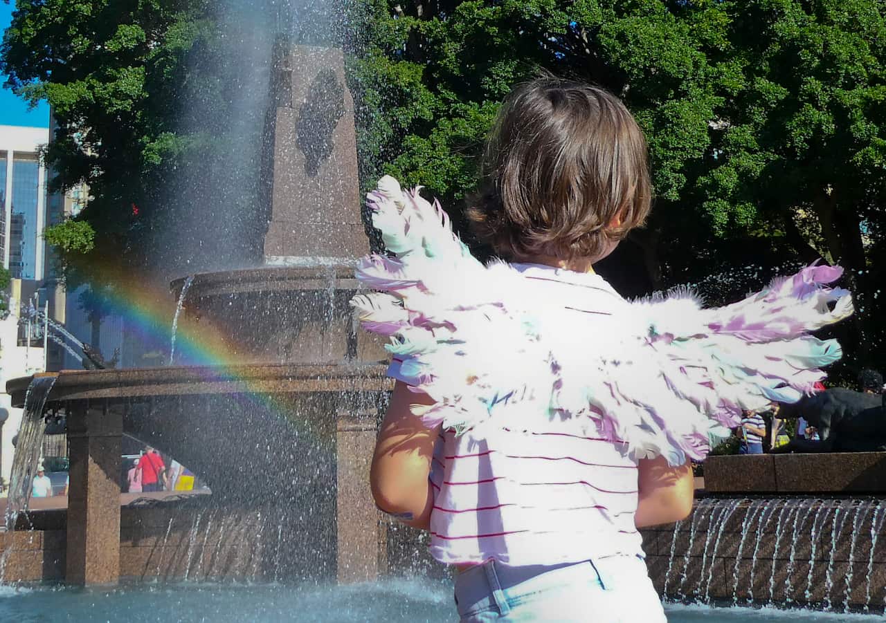 Child with angel wings in front of Hyde Park fountain.