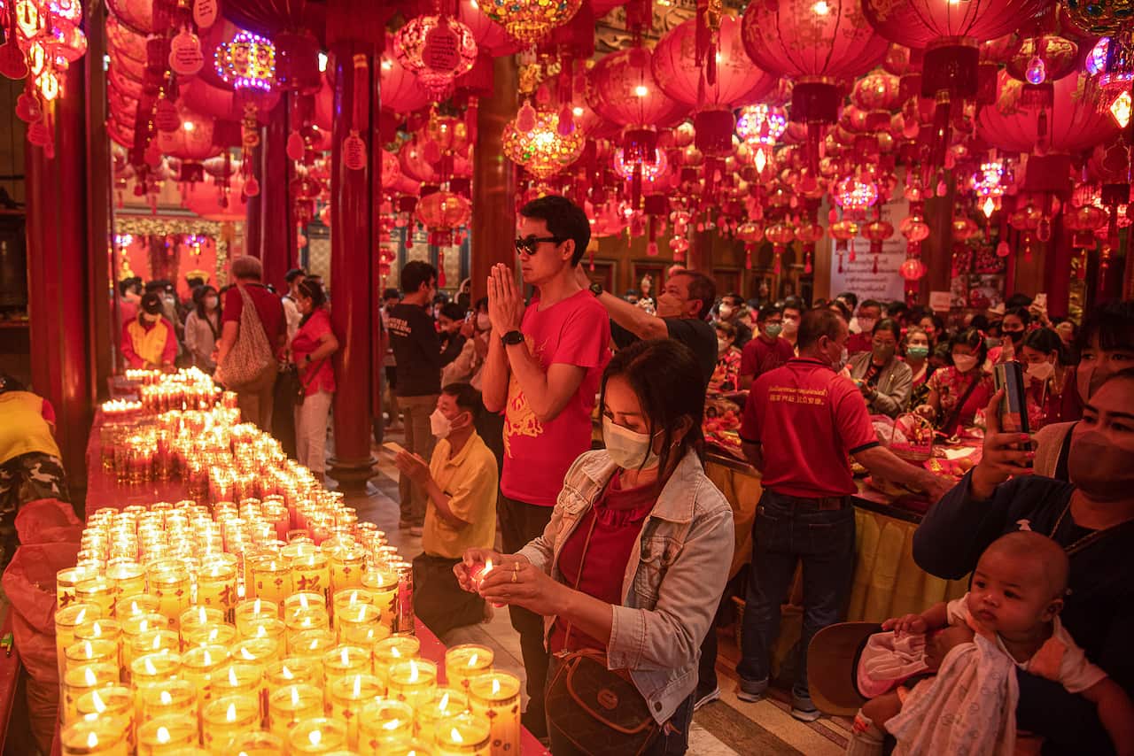 A woman lights a candle as lots of other people pray.