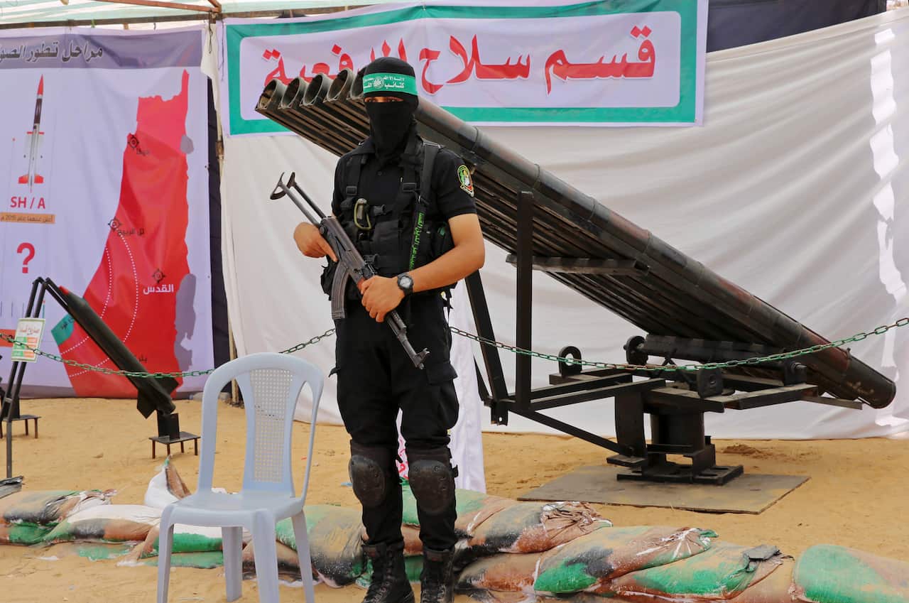 A person holding a rifle clad in black clothing, a black mask and a green headband with Arabic writing on it. 