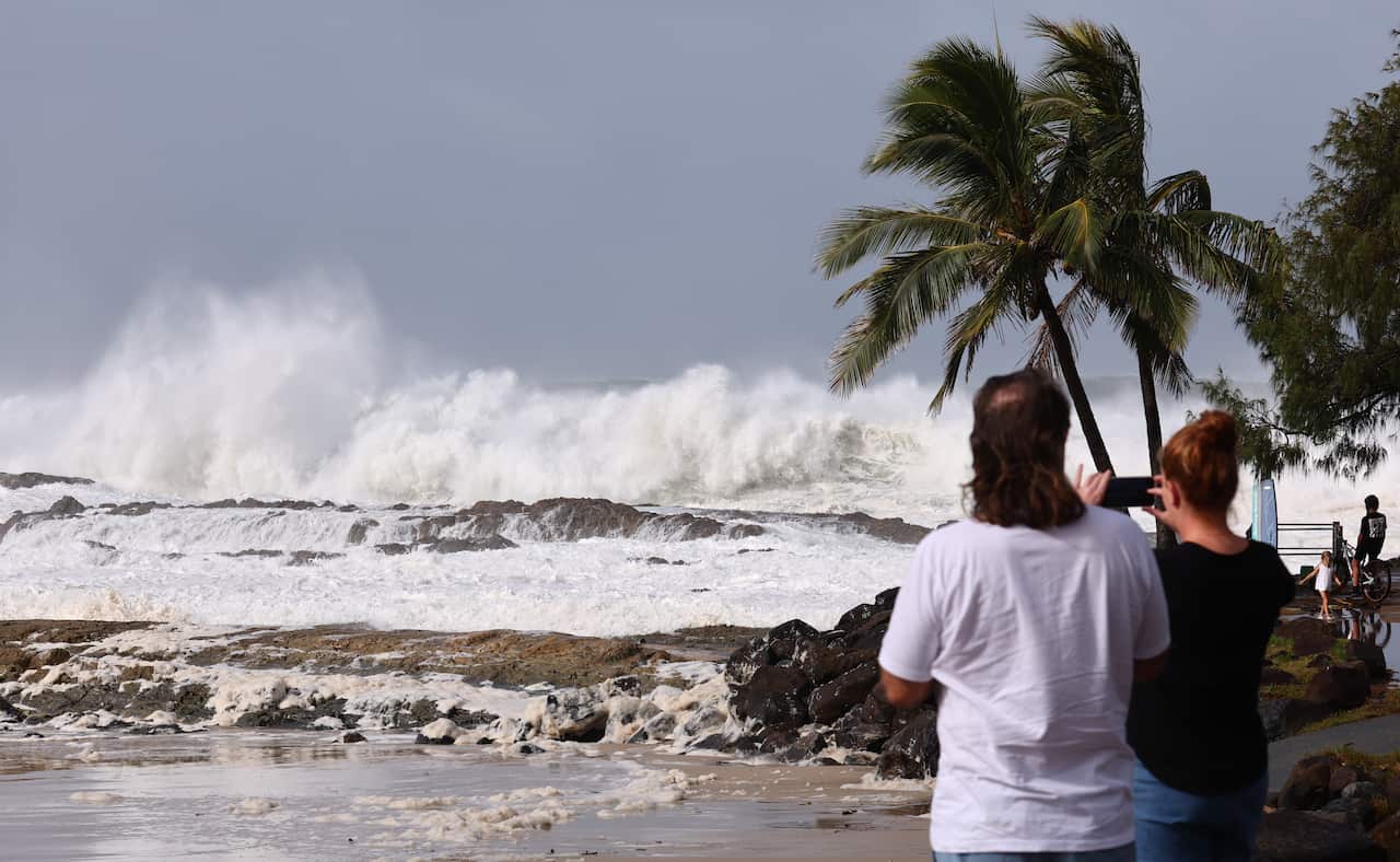 People looking out at the ocean where there are large waves crashing over rocks.