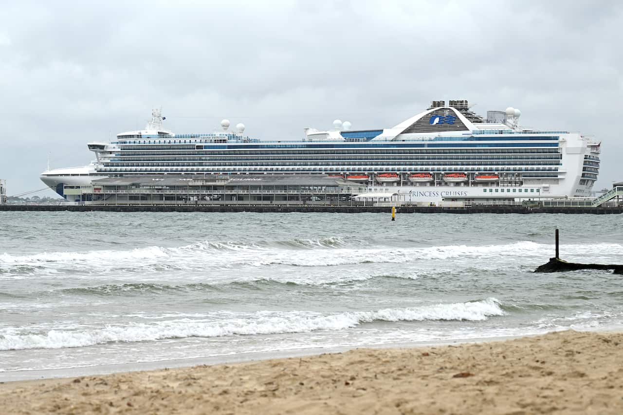 The Grand Princess Hamilton cruise ship docked at Station Pier in Melbourne, with a beach and waves in the foreground.