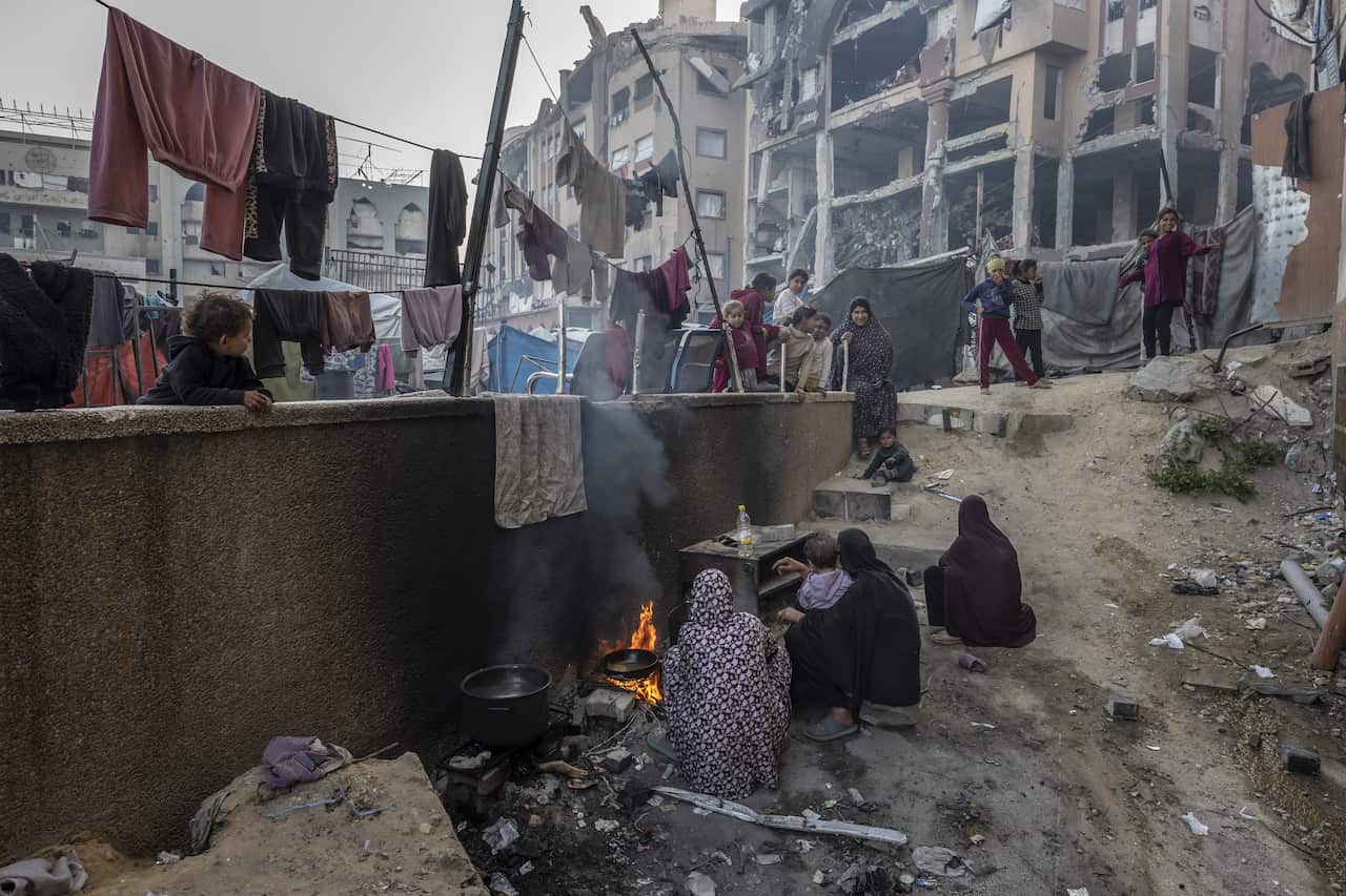 Edificios destruidos rodean a un grupo de mujeres cocinando comida sobre un fuego.