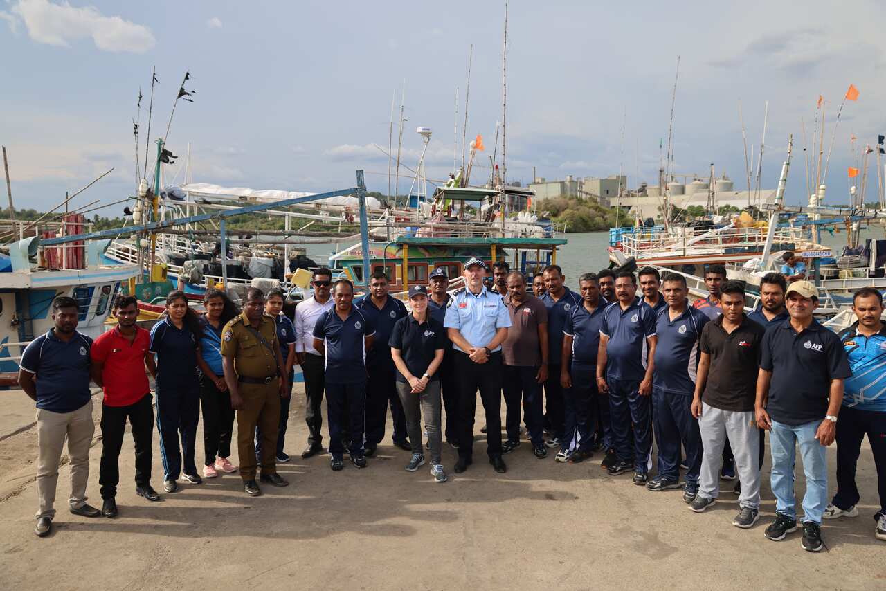 People in polo shirts and two men in police uniform stand pose in a group, colourful boats behind them