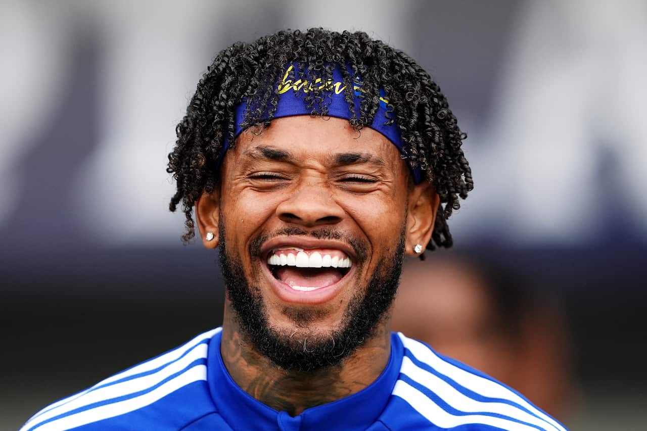 A close up shot of a man smiling widely with his eyes closed. He is wearing a blue jersey and a blue headband. 
