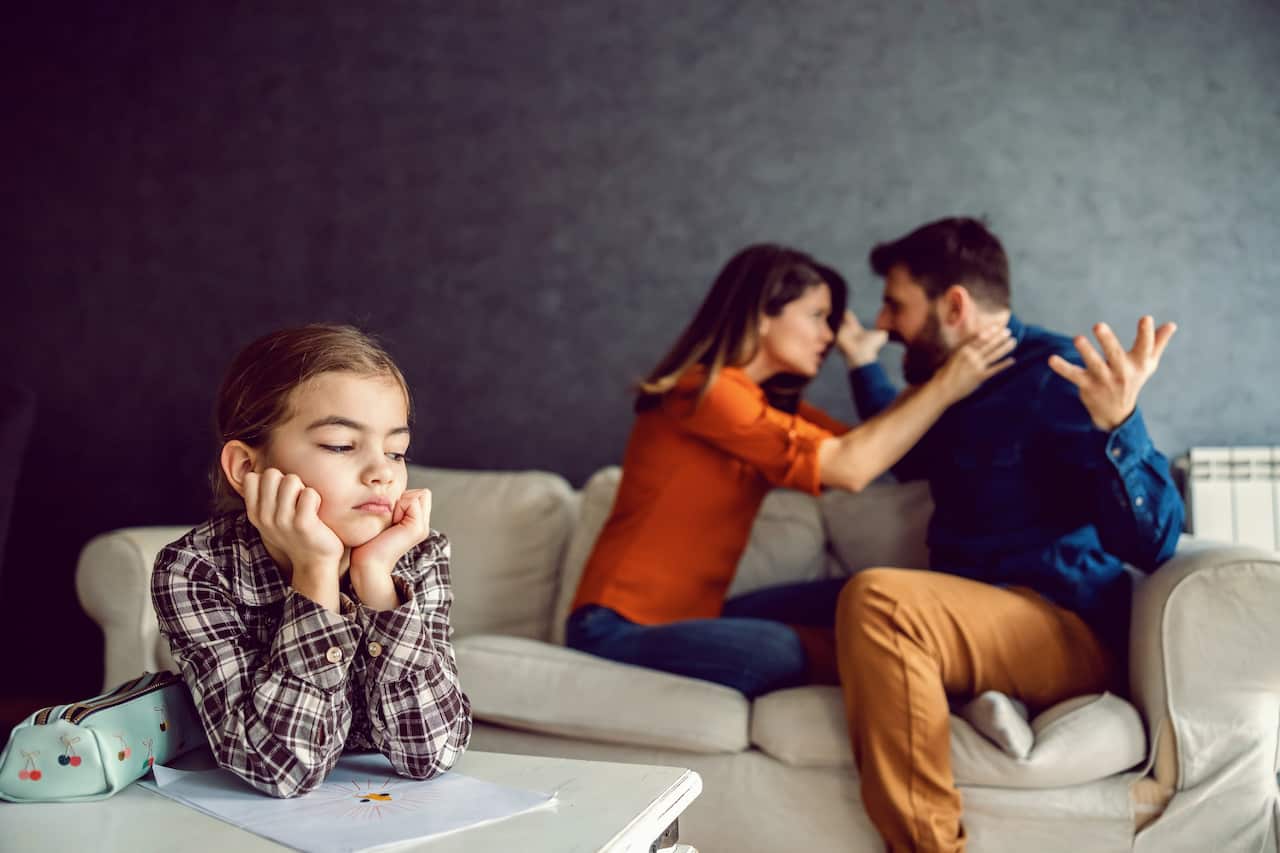 Sad little girl leaning on the desk and listening to parents arguing and yelling. It's not healthy for child to listen to quarrel. Parents must think about healthy childhood.