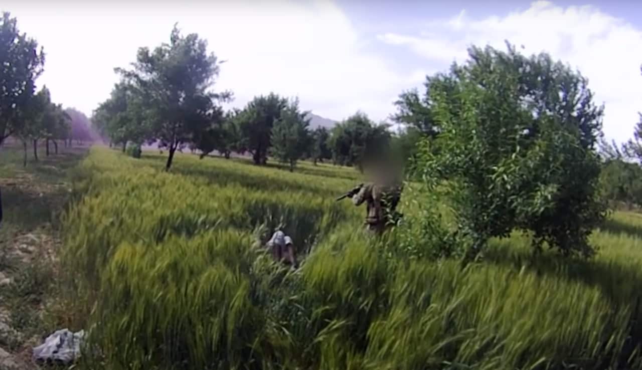 Screen shot of a soldier pointing a gun at a man in a wheat field.