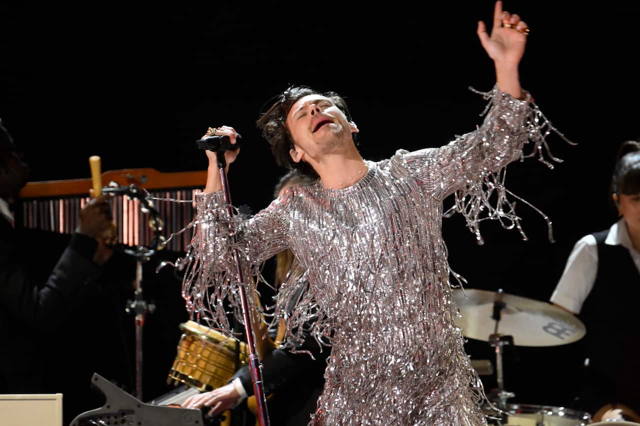A man who is wearing a silver jumpsuit singing on stage.