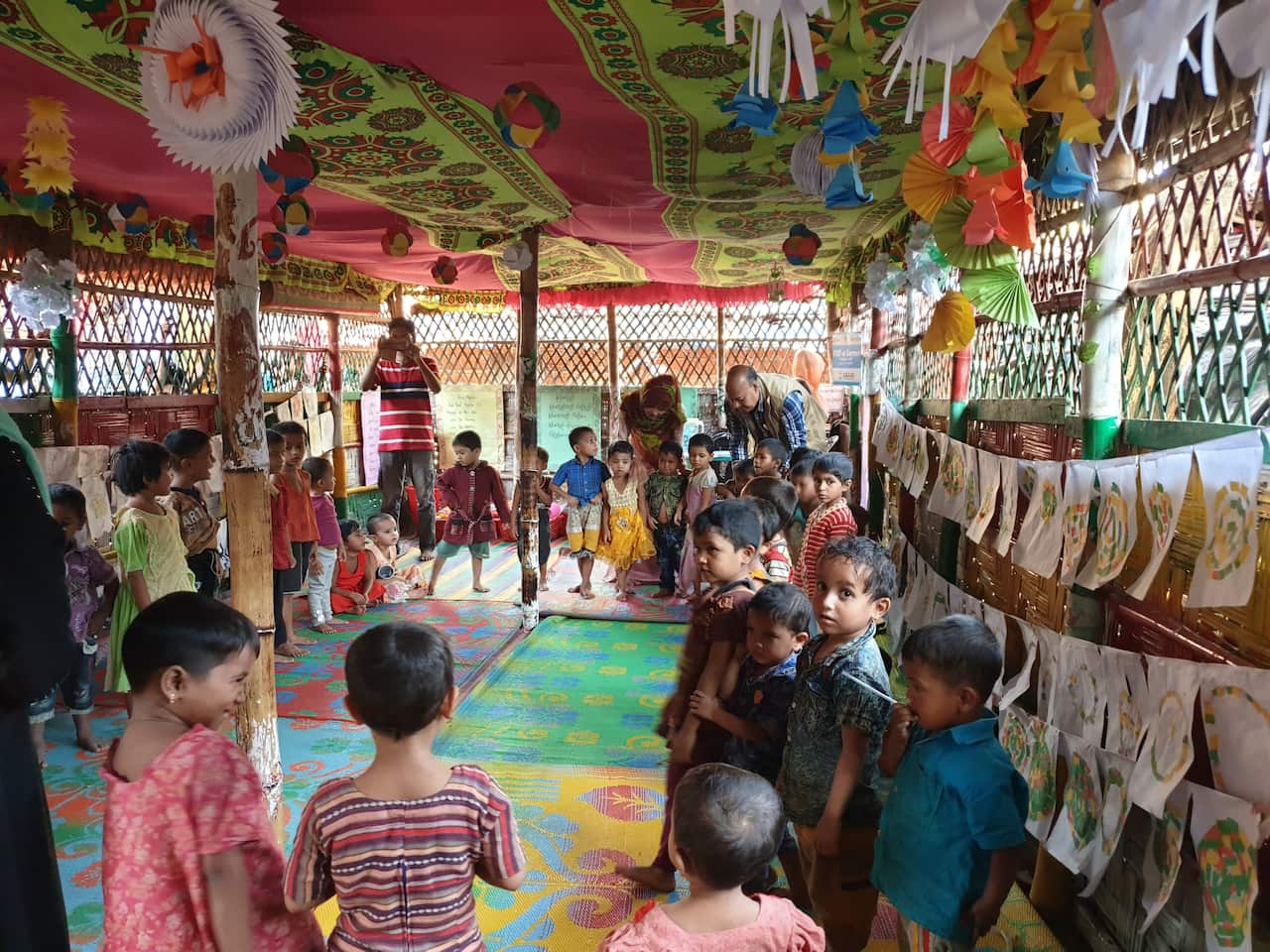 Children stand altogether in a colourful classroom. 