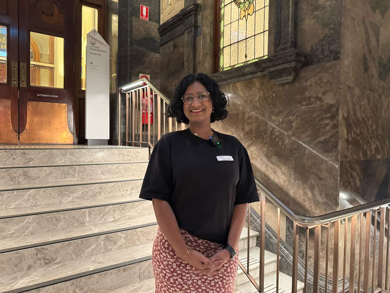 A woman smiling inside a building. There are steps behind her.