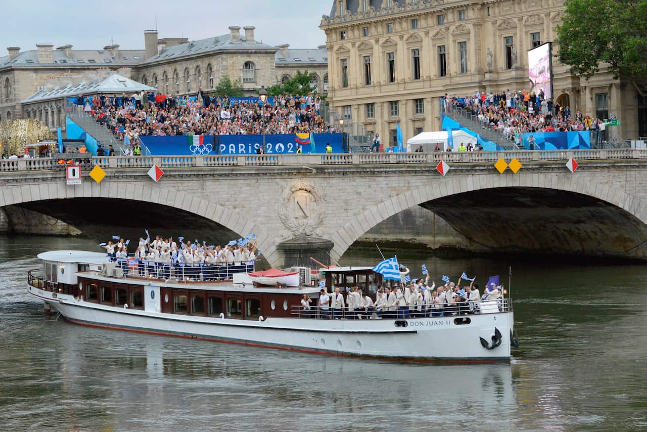 A boat on the river Seine with people holding Greek flags.