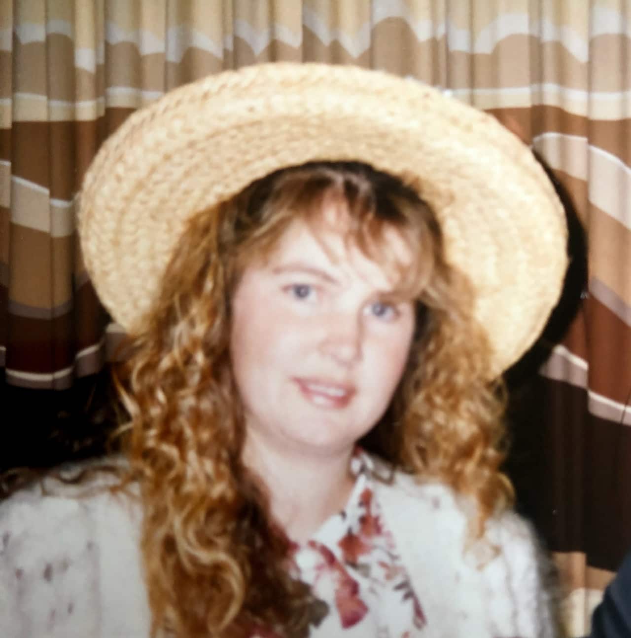 A young woman with long hair and a straw hat looks at the camera with a neutral expression.