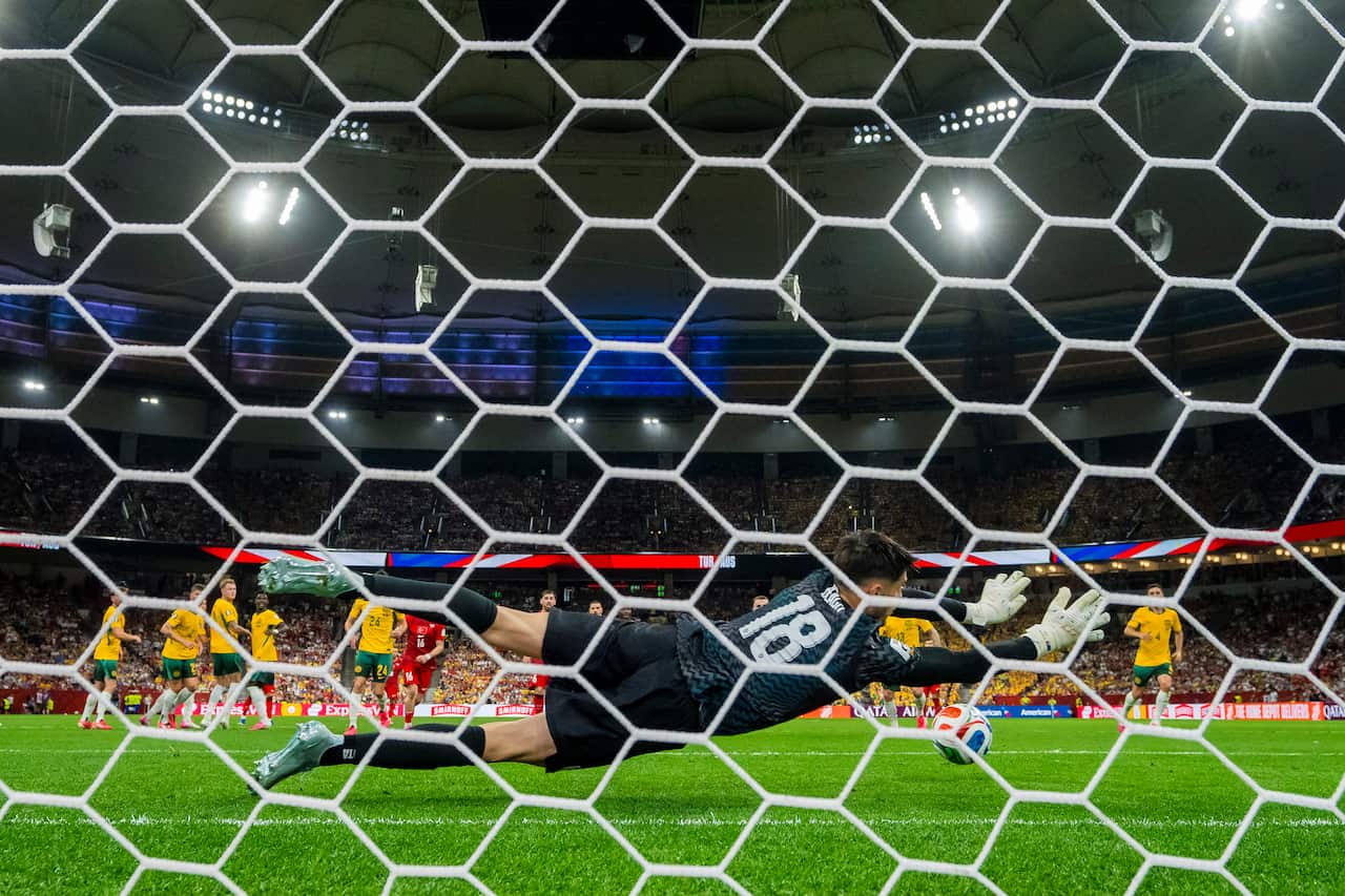 A view through the net of a goalkeeper in black uniform diving to his right about to make a save