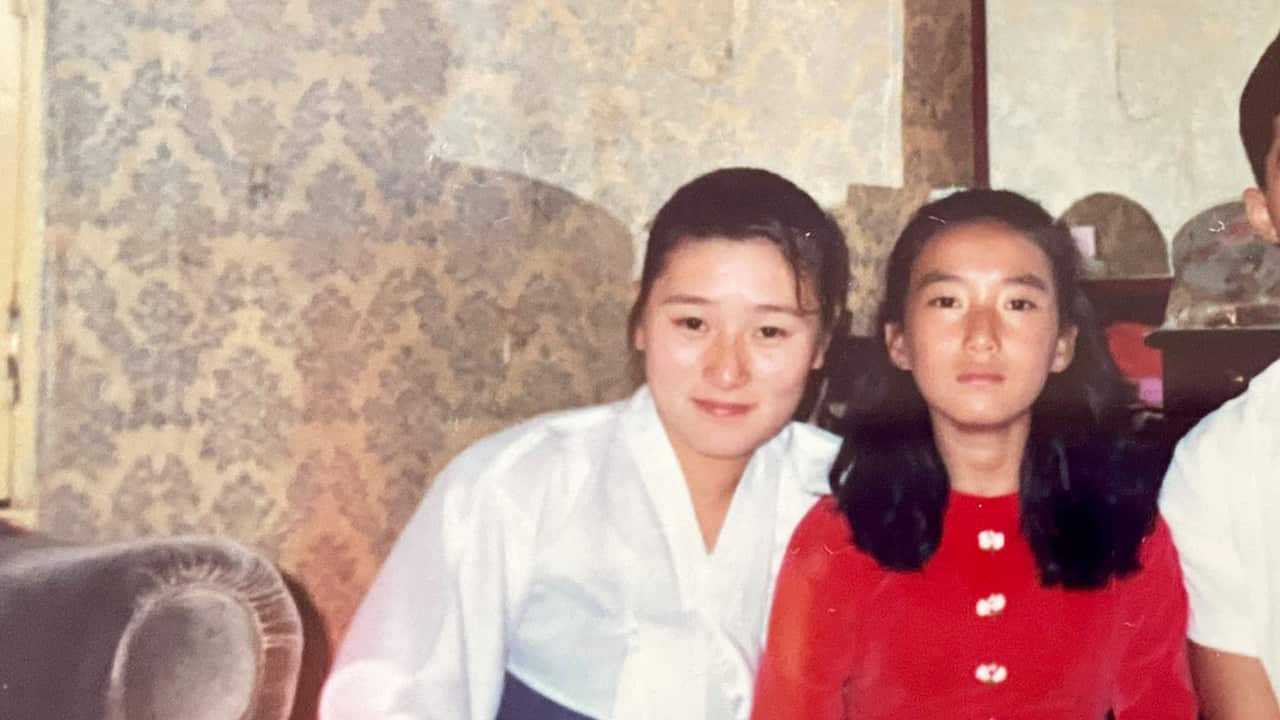 A Korean girl in a traditional dress posting for a photo next to a younger girl in a red dress