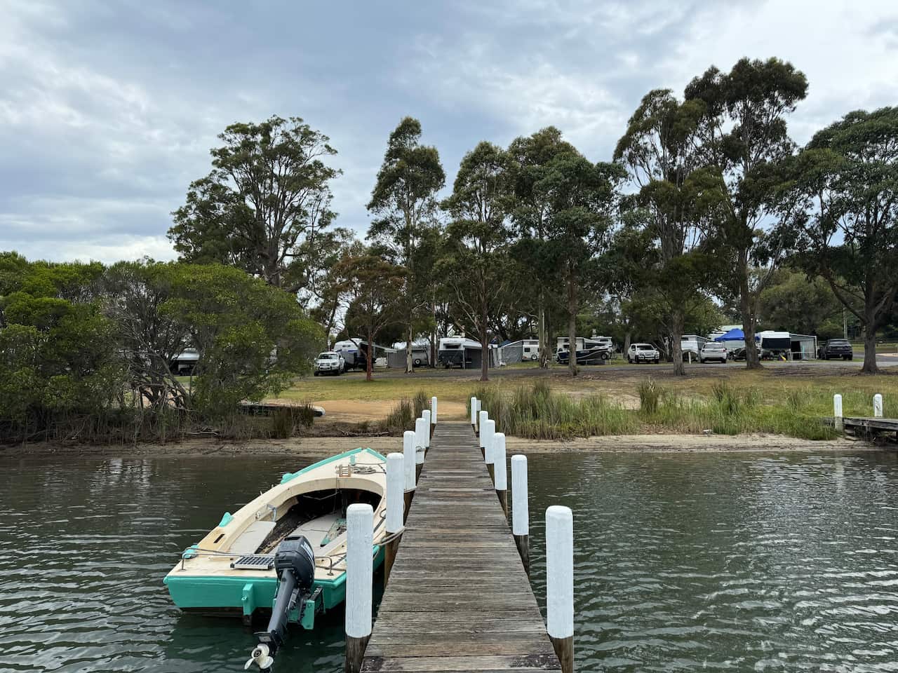 A boat is anchored next to a public jetty, surrounded by water with trees in the distance.