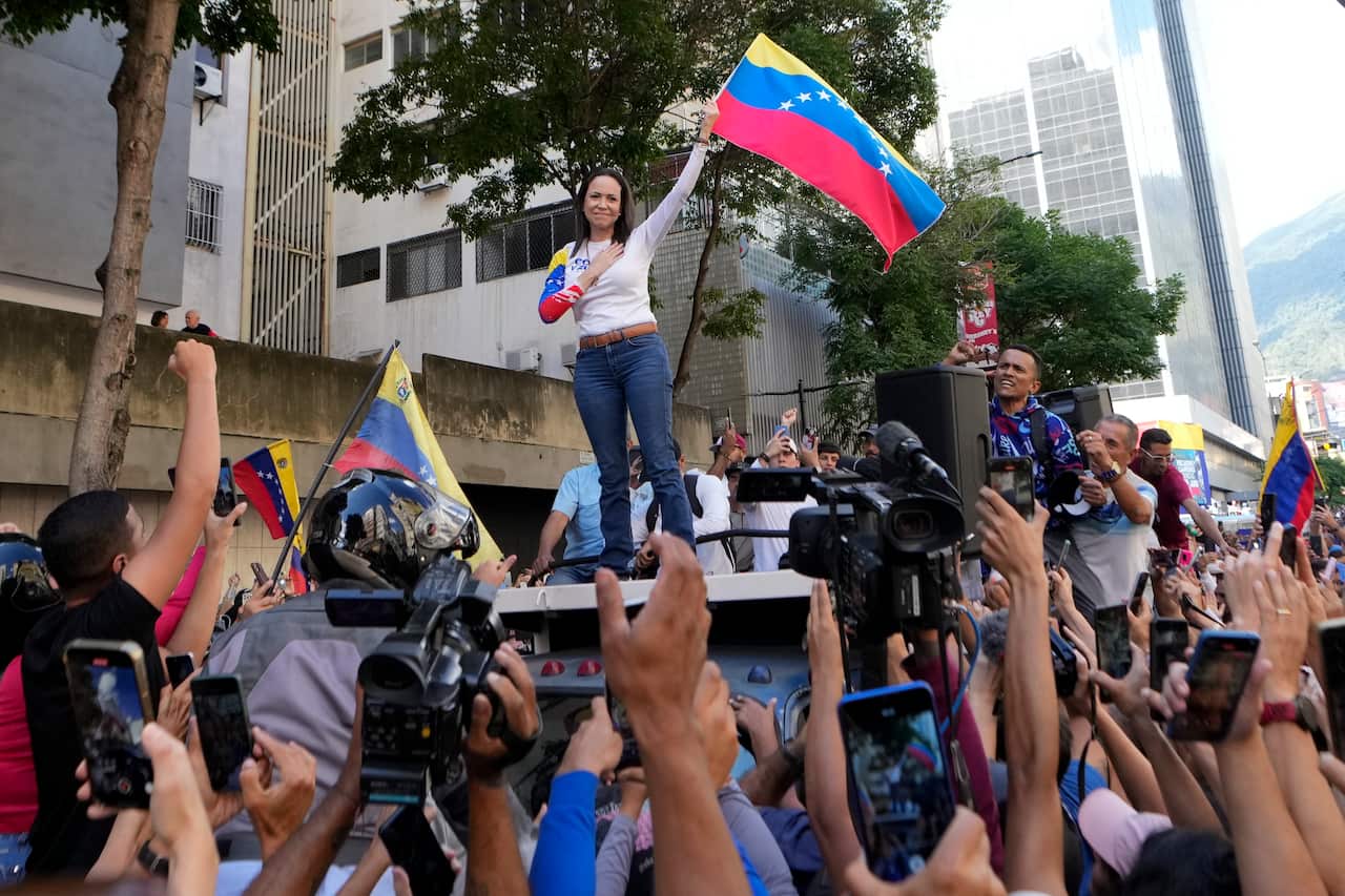 A woman stands on a car waving the Venezuelan flag in front of a crowd