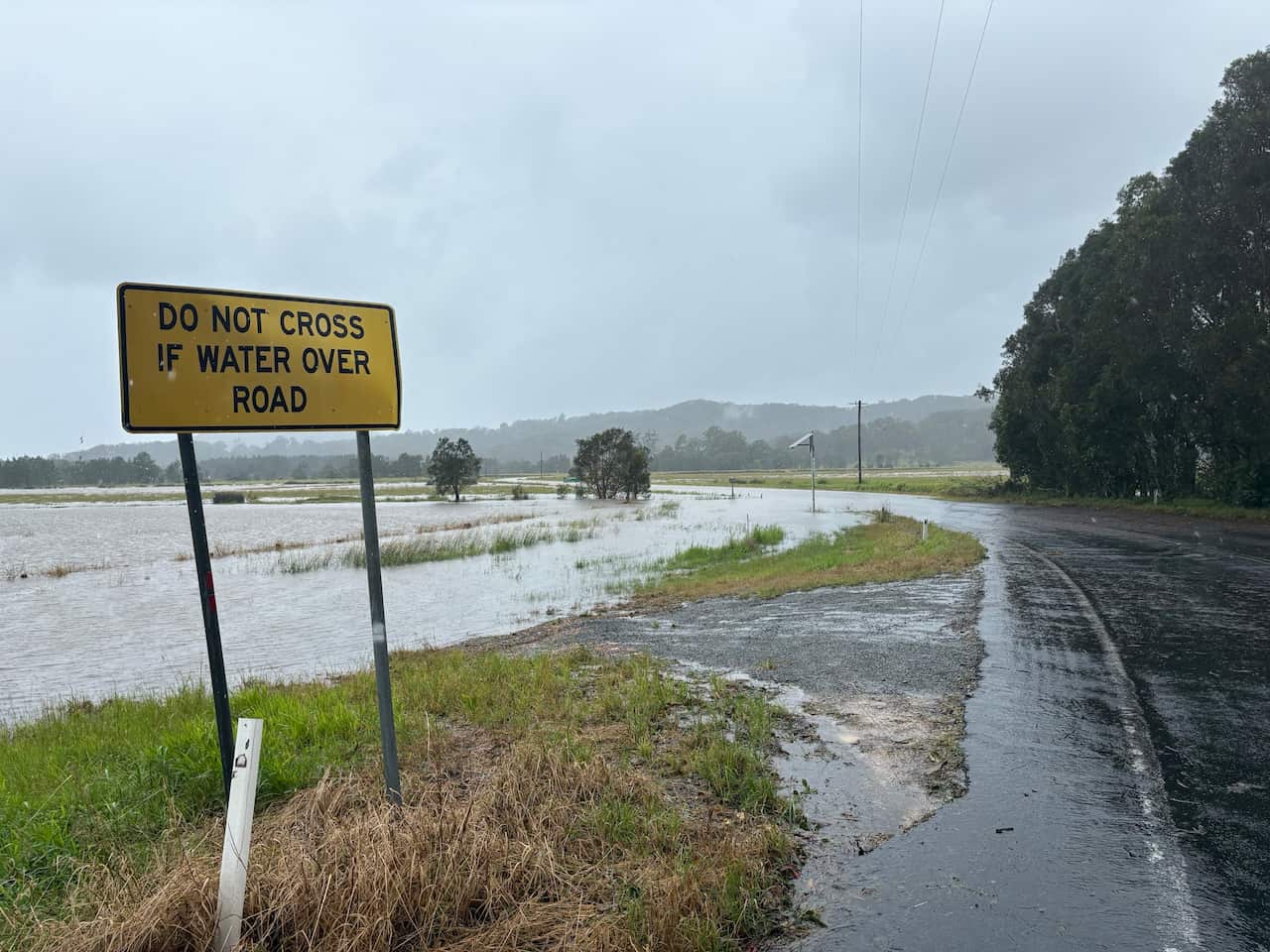 A flooded road next to a sign that warns against crossing dangerous terrain