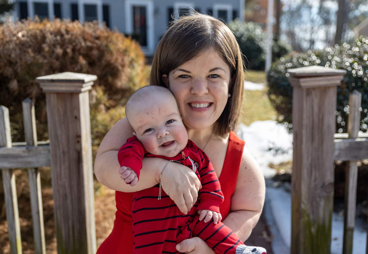 A smiling, brunette woman of short stature holds a smiling baby. They are both wearing red. 
