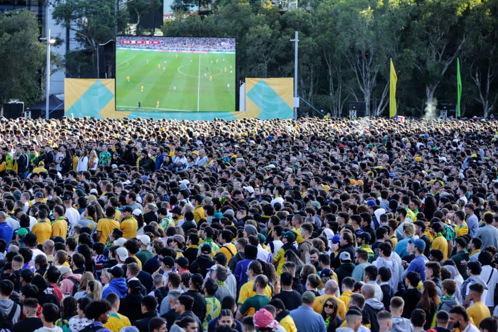 A large crowd watching a big television screen outdoors