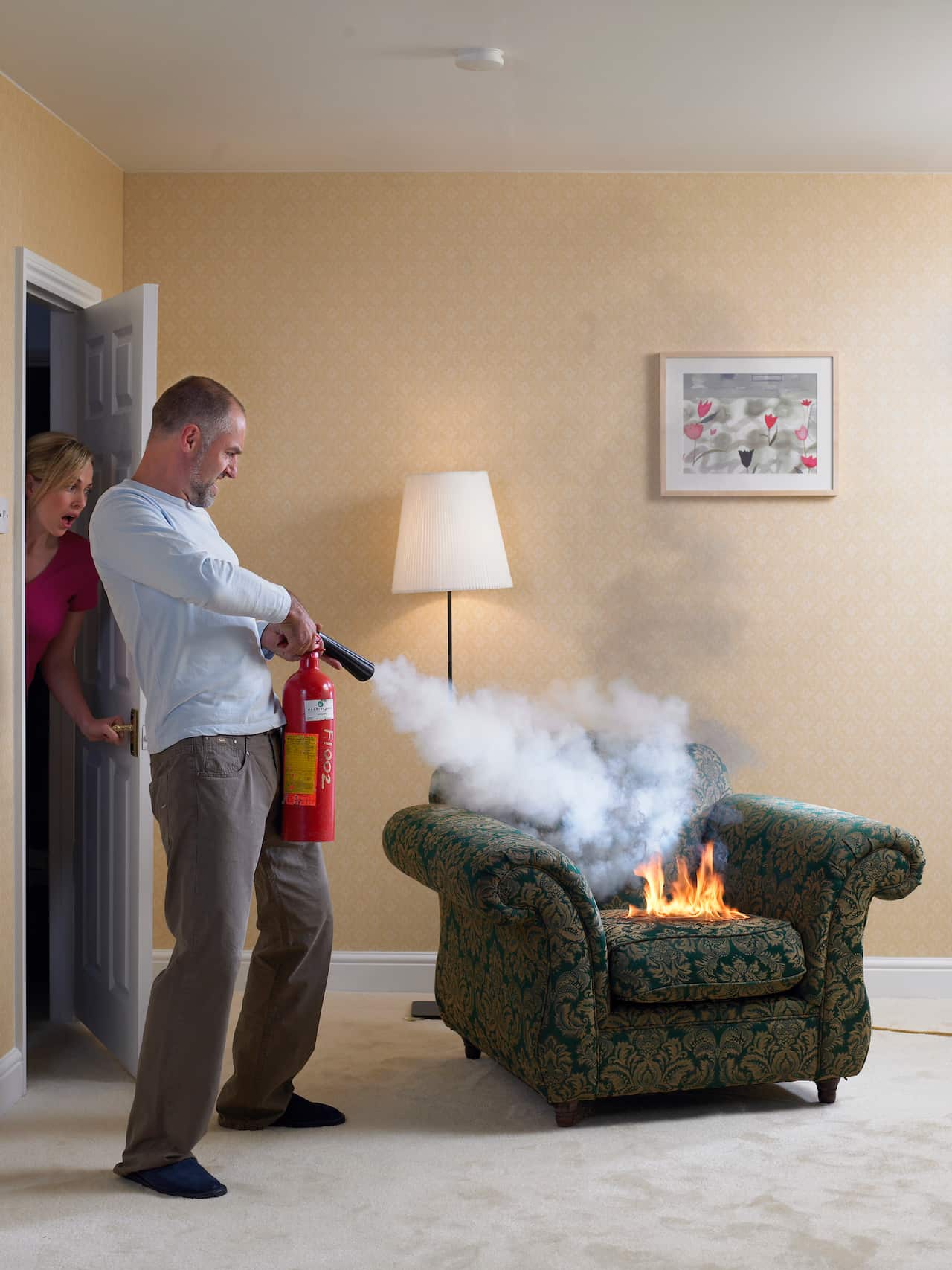 Man using fire extinguisher on arm chair on fire