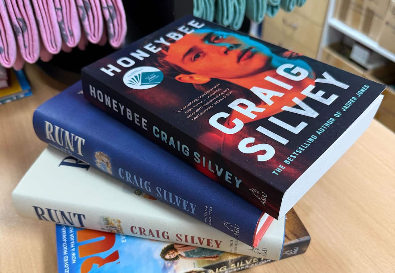 A stack of four books by author Craig Silvey, including Honeybee and two editions of Runt, rests on a wooden surface.