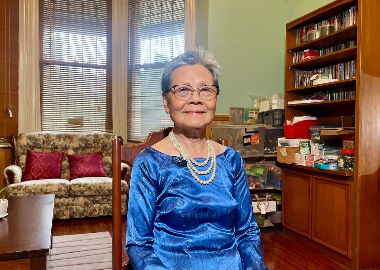 A woman in a blue dress and wearing glasses looks at the camera.
