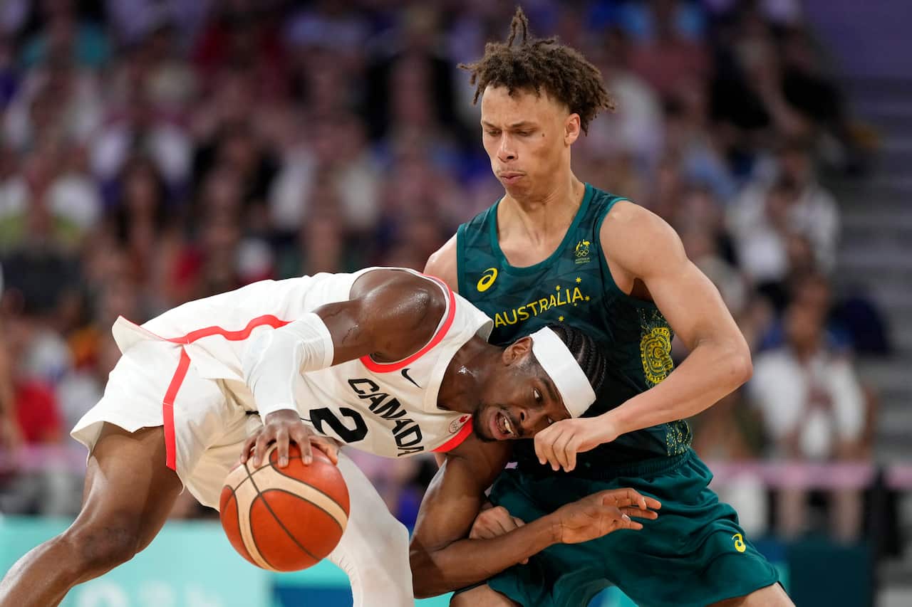 Two men playing basketball. One in a white uniform is shielding the ball from another in a dark green uniform.