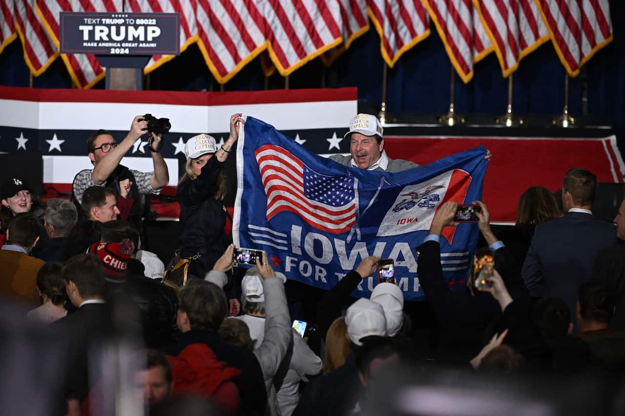 People cheer as a man holds a flag that reads "IOWA FOR TRUMP".