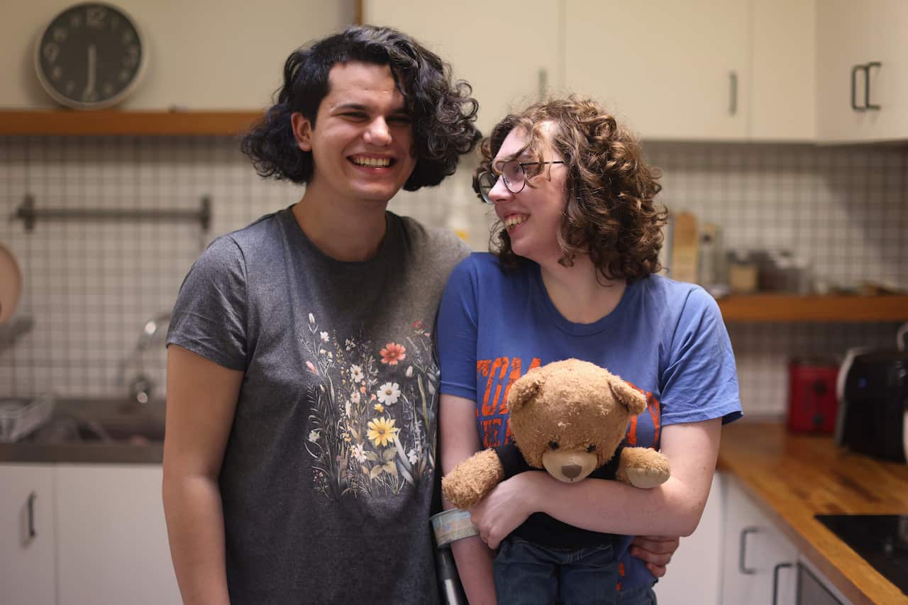 Two women standing together in a kitchen. Both are wearing t-shirts and one is holding a teddy bear